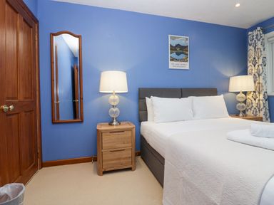 A bedroom with a double bed two bedside tables with lamps a mirror and blue walls at Fairfield View in Ambleside