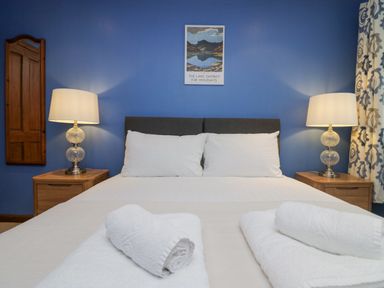 A bedroom with a double bed two rolled towels bedside tables with lamps a wall mirror and a framed picture at Fairfield View in Ambleside