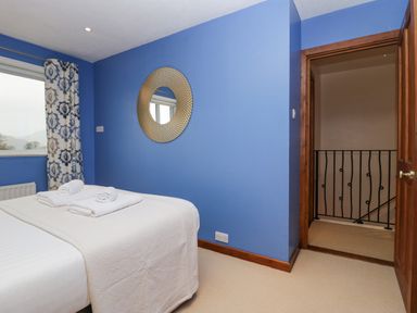 A bedroom with blue walls a bed with white linens towels on top a round mirror and a door leading to a hallway at Fairfield View in Ambleside