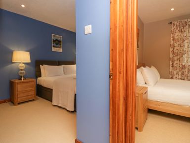 Two bedrooms with beds, bedside tables and lamps separated by a blue wall at Fairfield View in Ambleside