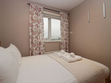 A bedroom with a bed made with white linens and folded towels on top next to a window with floral curtains at Fairfield View in Ambleside