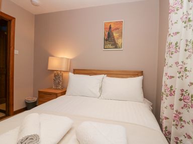 A bedroom with a bed white pillows a wooden bedside table lamp floral curtains and a wall poster at Fairfield View Ambleside