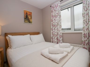 A bedroom with a bed with white linens and towels on top floral curtains and a window at Fairfield View in Ambleside