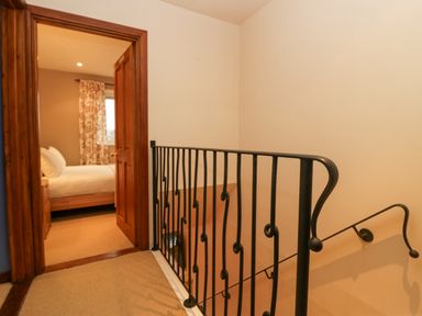 A hallway with a black metal railing and an open door leading to a bedroom with a bed and floral curtains at Fairfield View in Ambleside