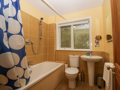A bathroom with a bathtub shower with blue and white curtain a toilet a pedestal sink and a frosted window at Fairfield View in Ambleside