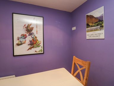 A corner of a room with purple walls a wooden chair a rectangular table a map of the British Isles and a Lake District holiday poster on the walls at Fairfield View in Ambleside