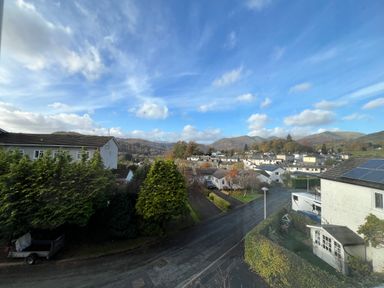 A residential area with houses trees and hills under a cloudy blue sky at Fairfield View in Ambleside