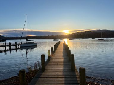 A wooden pier extending into a lake with sailboats moored and a sunset in the background at Fairfield View in Ambleside