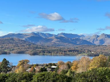 A view of a lake surrounded by trees and houses with mountains in the background at Fairfield View in Ambleside