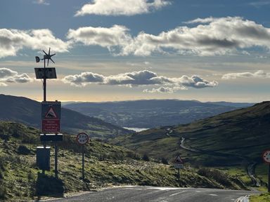 A winding mountain road with traffic signs and hills in the background at Fairfield View in Ambleside