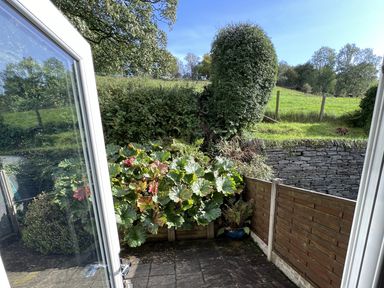 A patio with plants and a wooden fence overlooking a stone wall and grassy hill at Fairfield View Ambleside