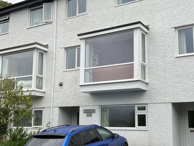 A blue car parked outside a white textured two-storey house with large windows at Fairfield View in Ambleside