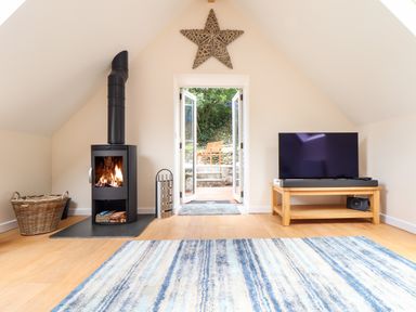 A room with a wood stove burning near a basket and a television on a wooden stand at Potters Barn in Trevarno near Helston