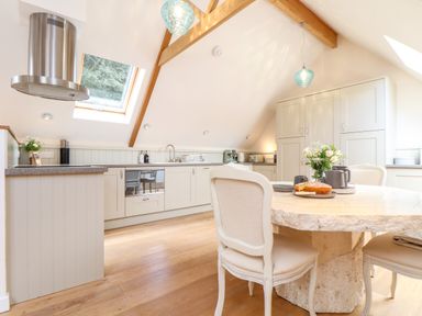 A kitchen with stone table and upholstered chairs wooden beams and skylight windows at Potters Barn in Trevarno near Helston
