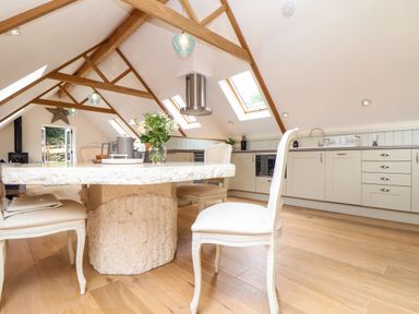 A kitchen with wooden beams skylights and a stone dining table at Potters Barn Trevarno near Helston