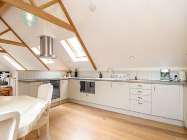 A kitchen with light-colored cabinets wooden beams on the ceiling and skylight windows at Potters Barn Trevarno near Helston