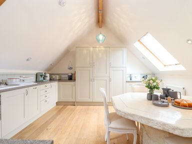 A kitchen with cabinetry a countertop an island table with chairs and a skylight at Potters Barn Trevarno near Helston