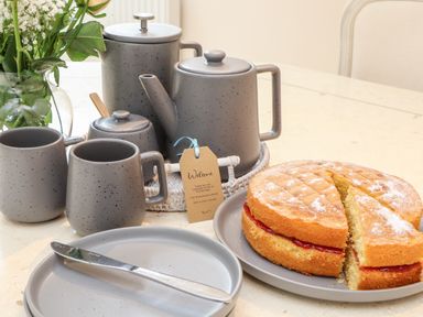 A table with grey ceramic teapots mugs plates a knife and a Victoria sponge cake at Potters Barn in Trevarno near Helston