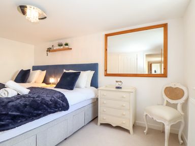 A bedroom with a bed with blue and white pillows a side table with a jar a mirror on the wall and a white chair at Potters Barn Trevarno near Helston