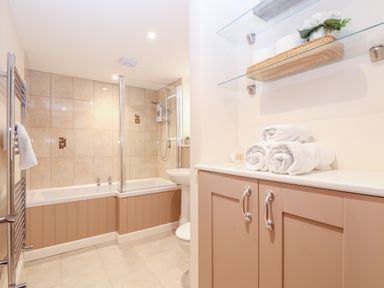 A bathroom with a bathtub shower combination towels on a counter and glass shelves at Potters Barn in Trevarno near Helston