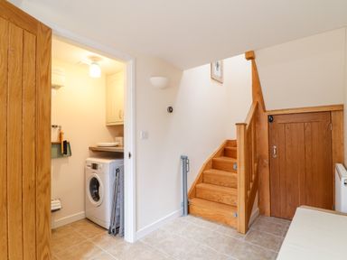 A laundry room with a washing machine next to wooden stairs and a small wooden door at Potters Barn Trevarno near Helston