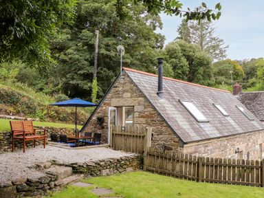 An outdoor patio with table chairs and umbrella next to a stone house with skylights and fenced yard at Potters Barn Trevarno near Helston