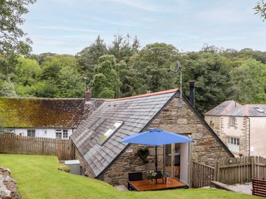 An outdoor patio with a table and blue umbrella next to a stone house with a sloped roof at Potters Barn in Trevarno near Helston