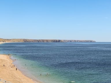A sandy beach with people swimming and walking near the water at Potters Barn in Trevarno near Helston