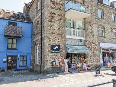 Stone building with a shop named Uncharted with toys outside next to a blue building with a balcony at 3 River View in Looe