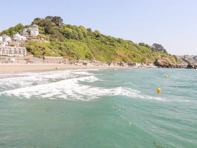 A coastal beach with green water waves and buildings on a hill at 3 River View in Looe