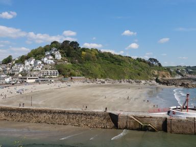 A beach with a sea wall and people walking on the sand near houses on a hillside at 3 River View in Looe