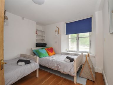 A bedroom with two beds and a bookshelf at 3 River View, Looe