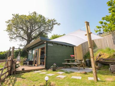 A small green cabin with a wooden deck chairs and a picnic table under a white canopy in a garden at Dart View Hideout in Totnes