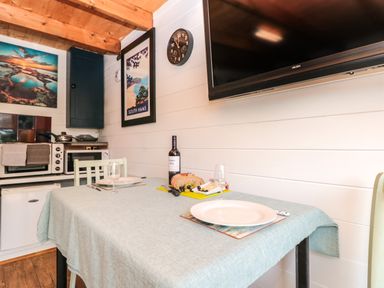 A small kitchen dining area with a table set for two and a wall-mounted TV at Dart View Hideout in Totnes