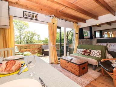 A living area with a table set for dining a wooden chest as a coffee table a green covered sofa with cushions and sliding doors opening to a wooden deck at Dart View Hideout in Totnes