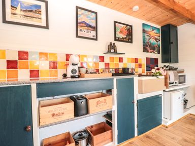 A kitchen countertop with colorful tiled backsplash wooden crates coffee maker toaster and framed pictures on the wall at Dart View Hideout in Totnes