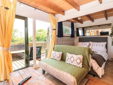 A room with a bed and a sofa in front of sliding glass doors with yellow curtains at Dart View Hideout in Totnes