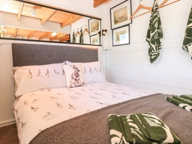 A bedroom with a bed linens featuring bird and rabbit designs and towels hanging on the wall at Dart View Hideout in Totnes