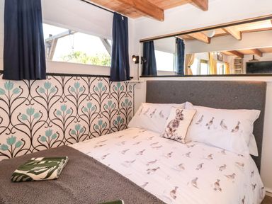 A bedroom with a bed with bird patterned bedding a decorative pillow with a rabbit design and a large mirror on the wall at Dart View Hideout in Totnes