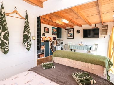 A studio apartment with a bed towels table and chairs kitchen area and wall mounted television at Dart View Hideout in Totnes