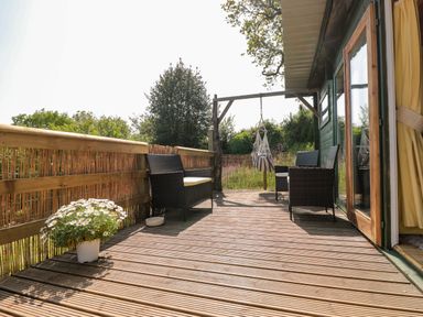 An outdoor wooden deck with wicker chairs a hanging chair a potted plant and wooden railing at Dart View Hideout in Totnes