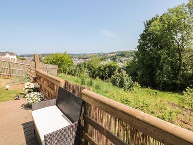 An outdoor deck with a wicker bench and a view of trees and a town at Dart View Hideout in Totnes