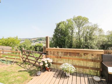 A wooden fenced garden area with flowers on a deck and trees in the background at Dart View Hideout in Totnes
