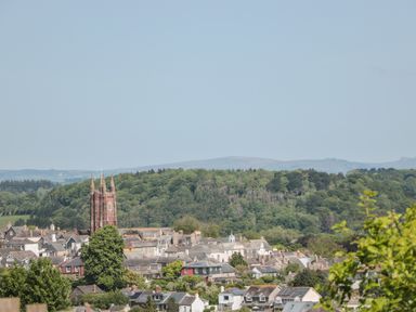 A town with a church tower surrounded by houses and trees with hills in the background at Dart View Hideout in Totnes