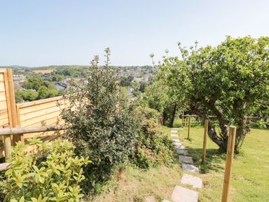 A grassy garden with a stone path wooden posts bushes and a tree overlooking a town at Dart View Hideout in Totnes