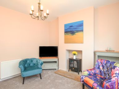 A living room with a blue armchair a floral armchair a black stove a television on a stand and a painting above the stove at The Skipper's House in Weymouth