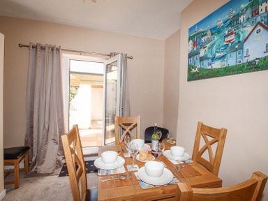 A dining room with a wooden table set for four with bowls glasses and a bottle with an open door and grey curtains at The Skipper's House in Weymouth