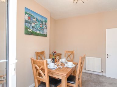 A dining room with a wooden table set for four with white bowls wine glasses and cutlery a painting on the wall and a radiator at The Skippers House in Weymouth