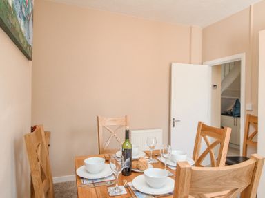 A dining room with a wooden table set for four with plates bowls glasses and a bottle of wine at The Skipper's House in Weymouth