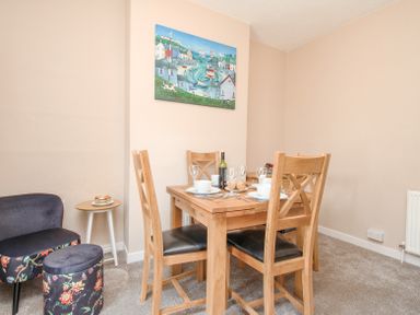 A dining area with a wooden table set for four and two floral upholstered stools with a small round side table at The Skipper's House in Weymouth